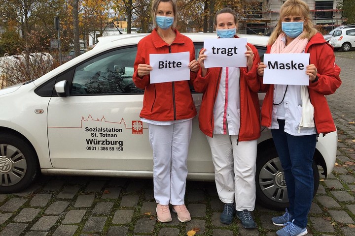 Mitarbeiter*innen halten Zettel "Bitte tragt Masken!" hoch. 